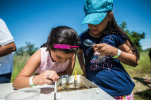 young girls performing science research with magnifying glasses